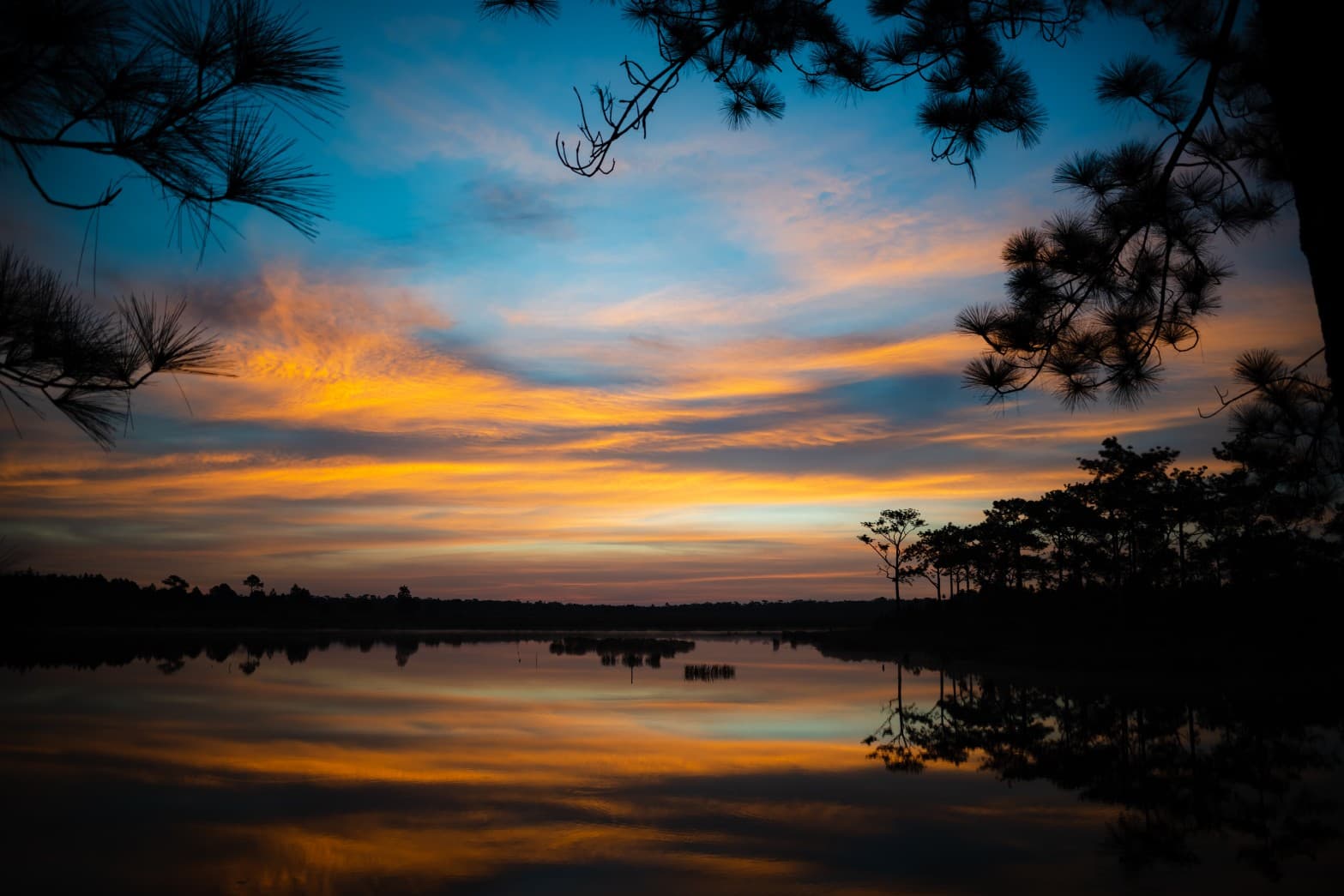 Calm lake reflecting colorful sunrise clouds at Phu Kradueng