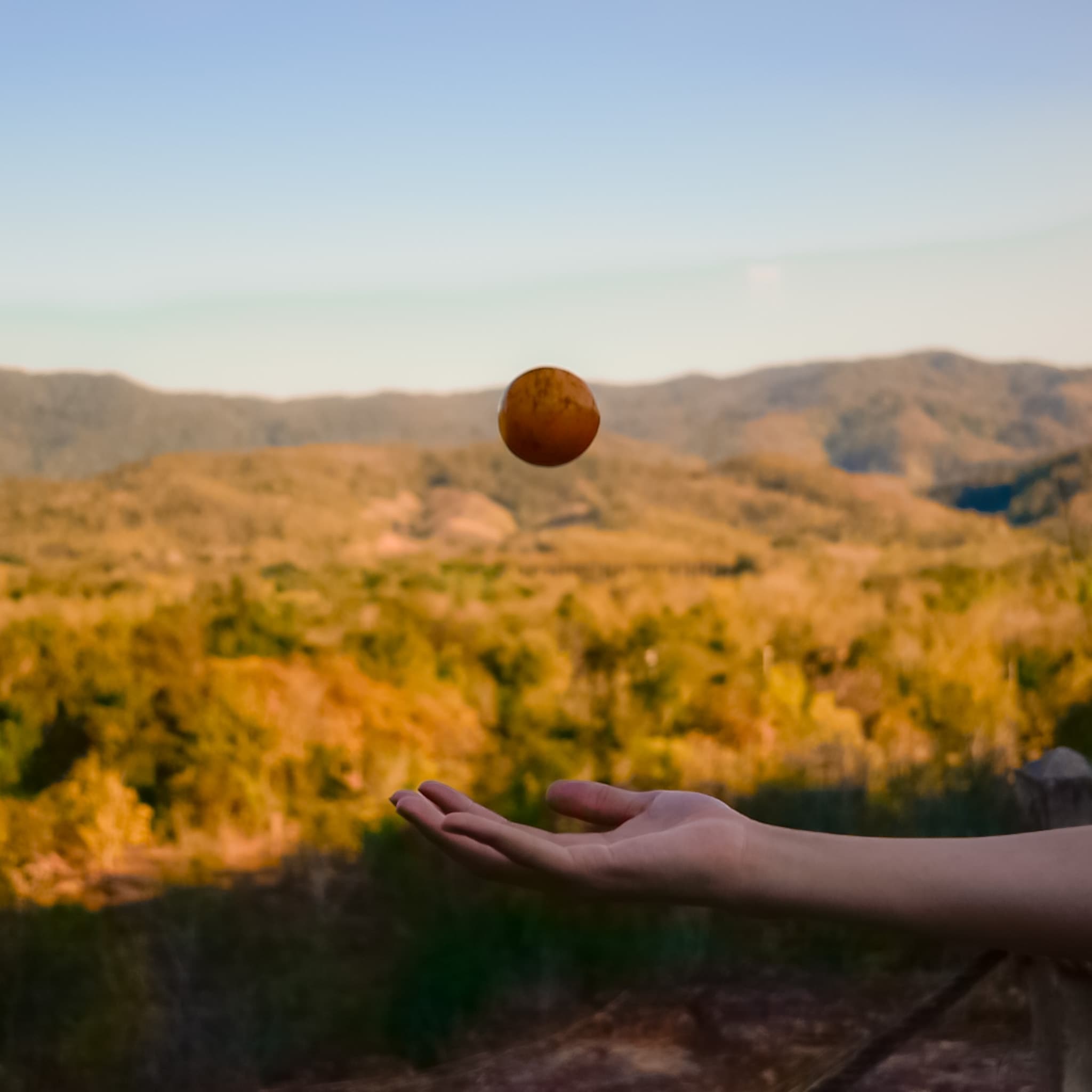 Hand tossing a small object with mountains behind